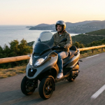 Homme souriant conduisant un scooter à trois roues sur une route sinueuse en bord de mer, illustrant la liberté de conduite avec un permis B